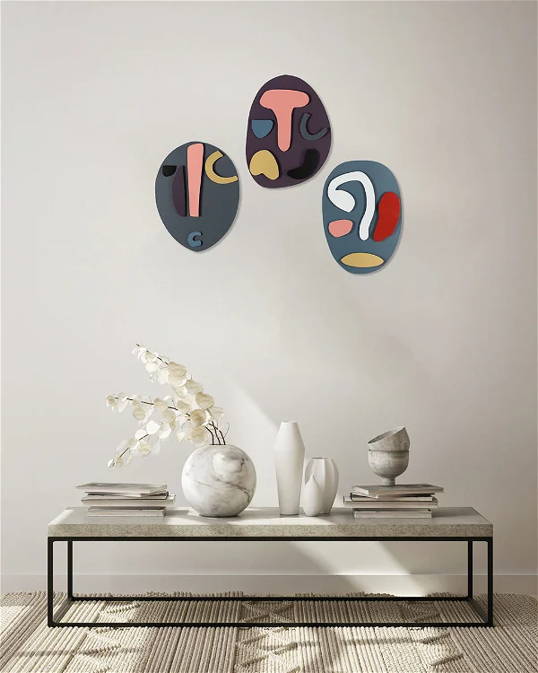 Three modern abstract paintings with bold shapes and soothing colors mounted on a white wall above a minimalist living room setup, enhancing contemporary home decor.