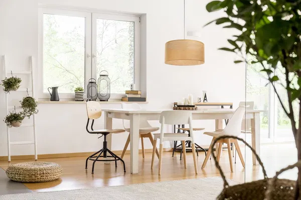 Bright dining area with white furniture, a wooden hanging lamp and green accents in front of large windows